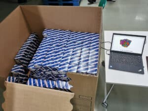 View of a filled shipping crate next to a laptop running an AI assisted packing software.