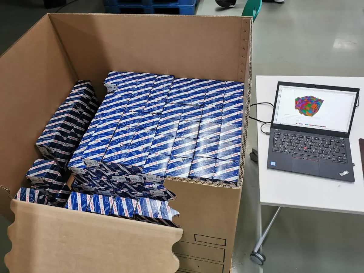 View of a filled shipping crate next to a laptop running an AI assisted packing software.