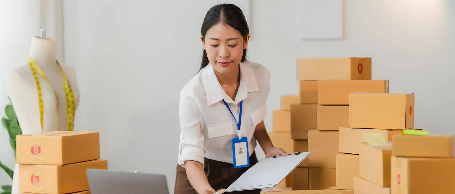 Eine asiatische KMU-Unternehmerin verwaltet sorgfältig Online-Bestellungen in ihrem Geschäft, umgeben von Versandkartons - Titelbild Integration des stationären Handels in die Wertschöpfungskette des E-Commerce