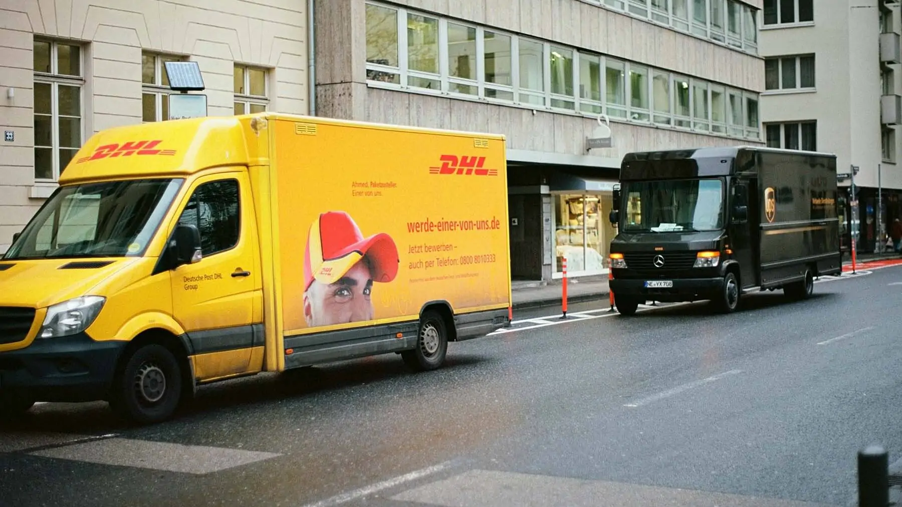Ein gelber DHL-Lieferwagen und ein brauner UPS-Lieferwagen parken in einer Straße - Foto von Markus Spiske - Unsplash-Code: EA5Ali_vISI
