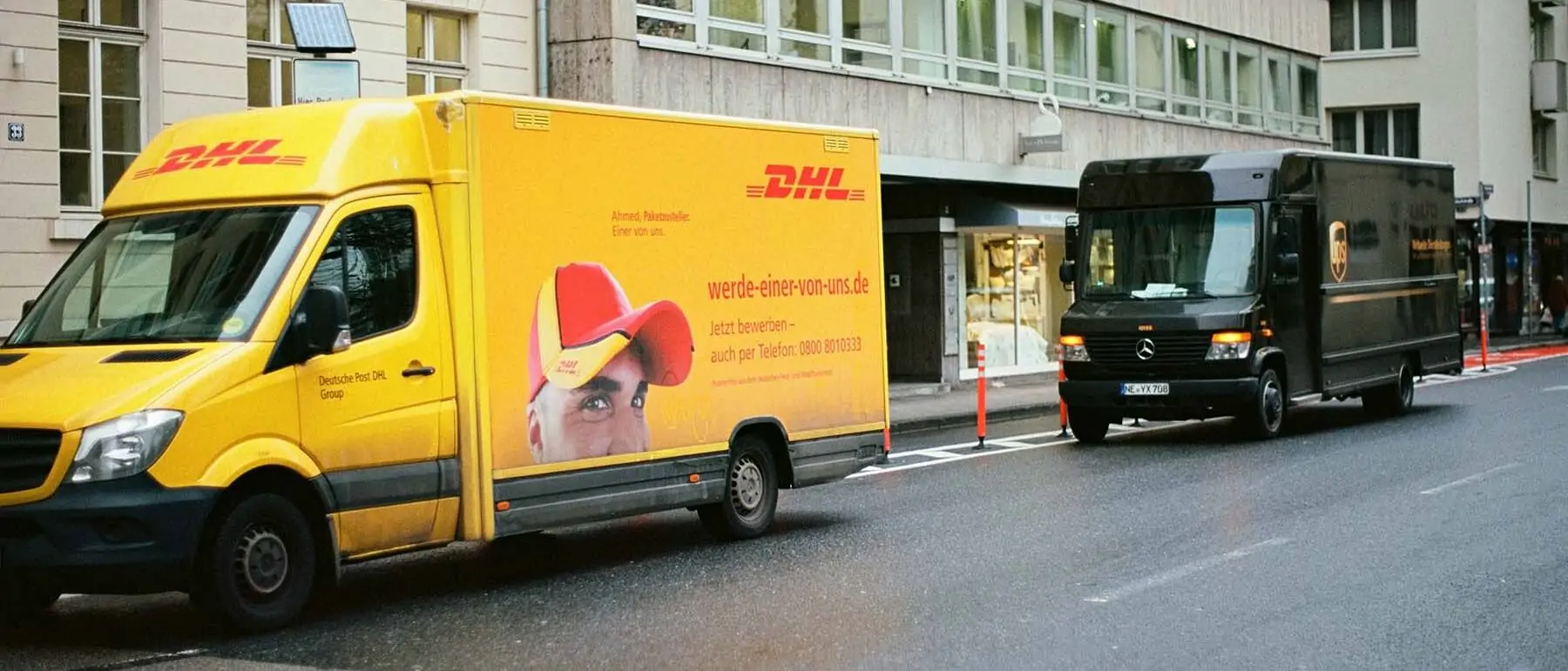 Ein gelber DHL-Lieferwagen und ein brauner UPS-Lieferwagen parken in einer Straße - Foto von Markus Spiske - Unsplash-Code: EA5Ali_vISI