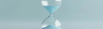 Sanduhr mit blauem Sand auf einem weichen blauen Hintergrund, die den Lauf der Zeit und die flüchtigen Momente des Lebens symbolisiert und die Bedeutung von Zeitmanagement und Reflexion betont