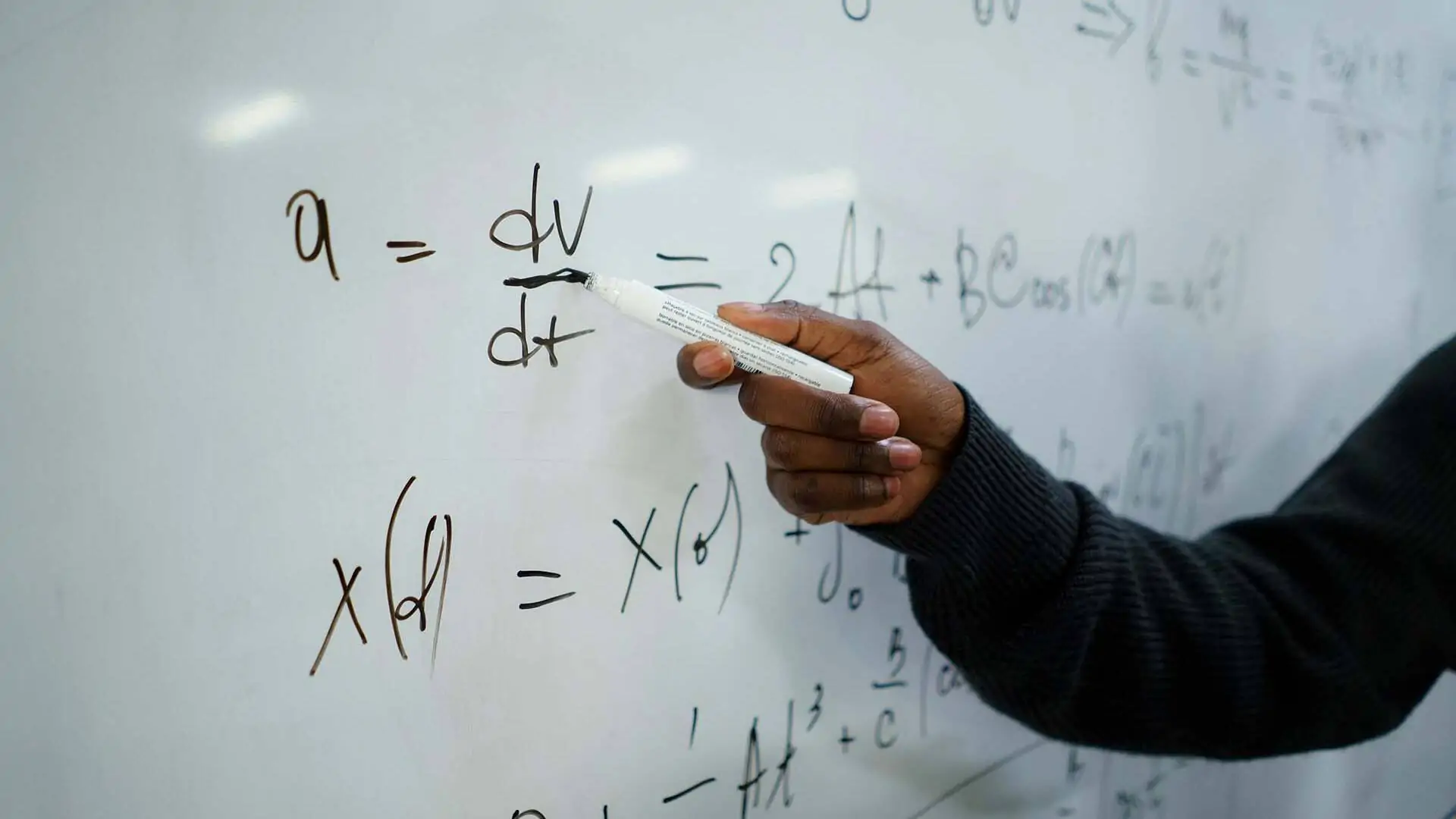 Person, die weißen Stift hält, der auf weiße Tafel schreibt, auf der eine mathematische Formel steht.