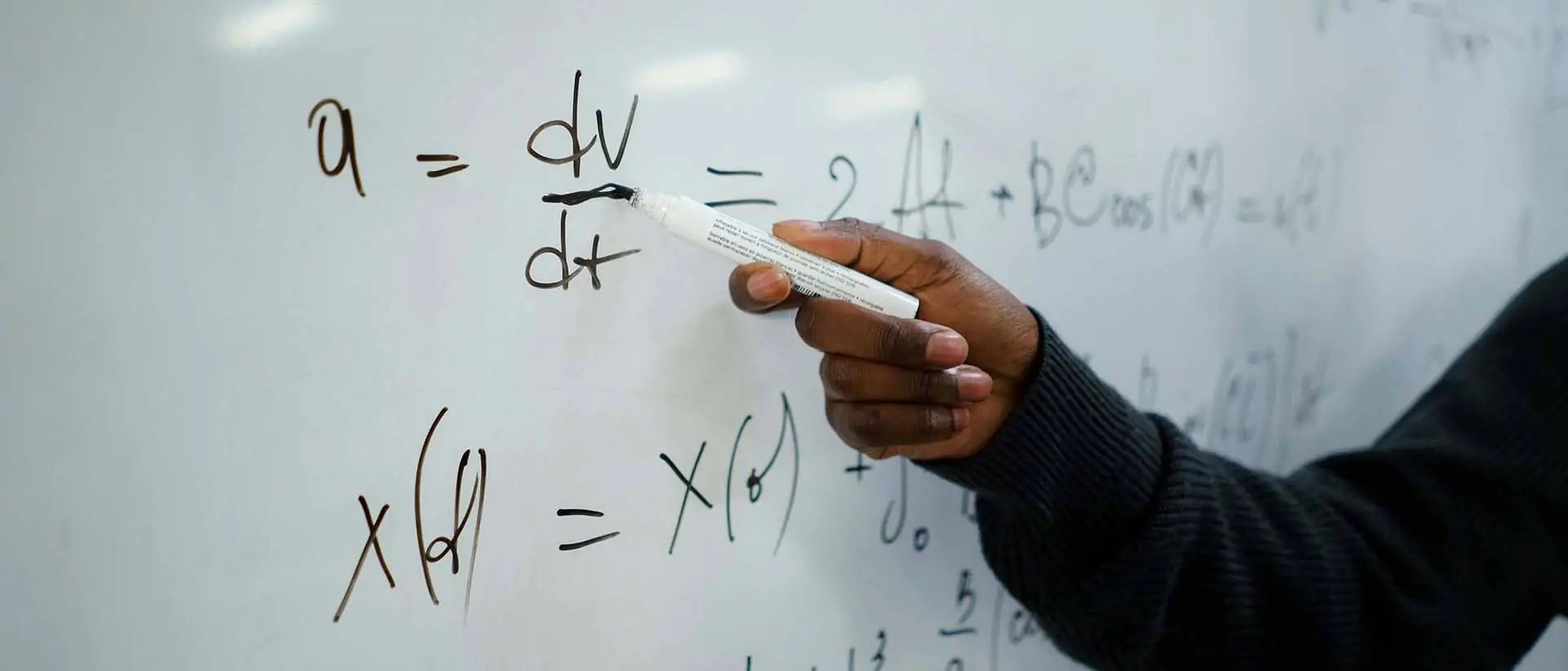 Person, die weißen Stift hält, der auf weiße Tafel schreibt, auf der eine mathematische Formel steht.