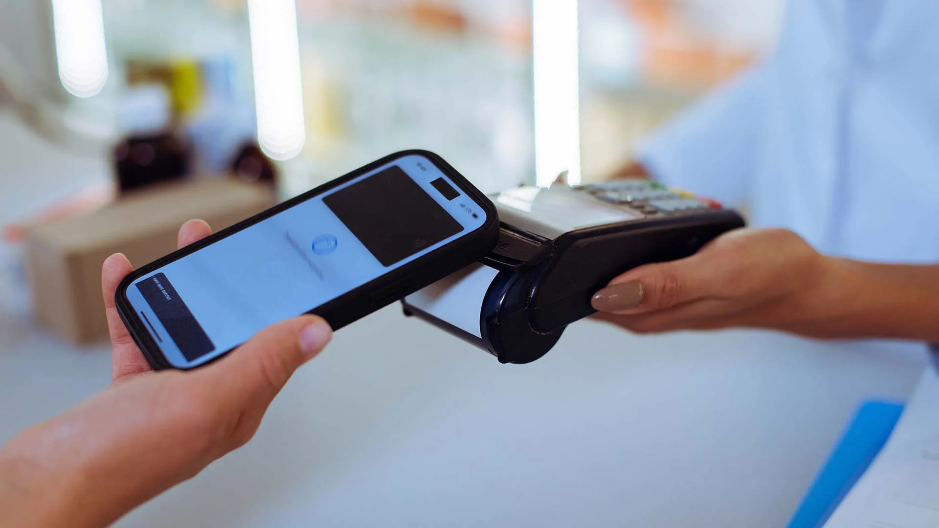 A hand holding a smartphone on the NFC reading area of a payment terminal held by another hand - the background is blurry
