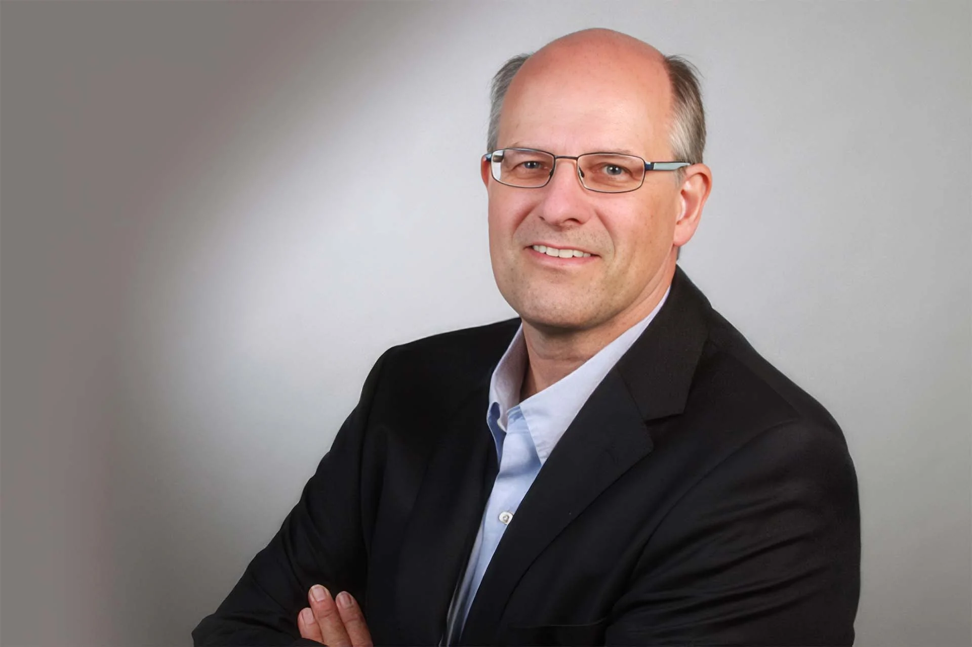 Portrait of Stefan Nie&szlig;en, operations manager at the Hermes fulfillment center in Haldensleben. Against a gray background, he smiles at the camera with his arms crossed. He is wearing an anthracite-colored jacket and a white shirt. Image copyright: Hermes Fulfilment