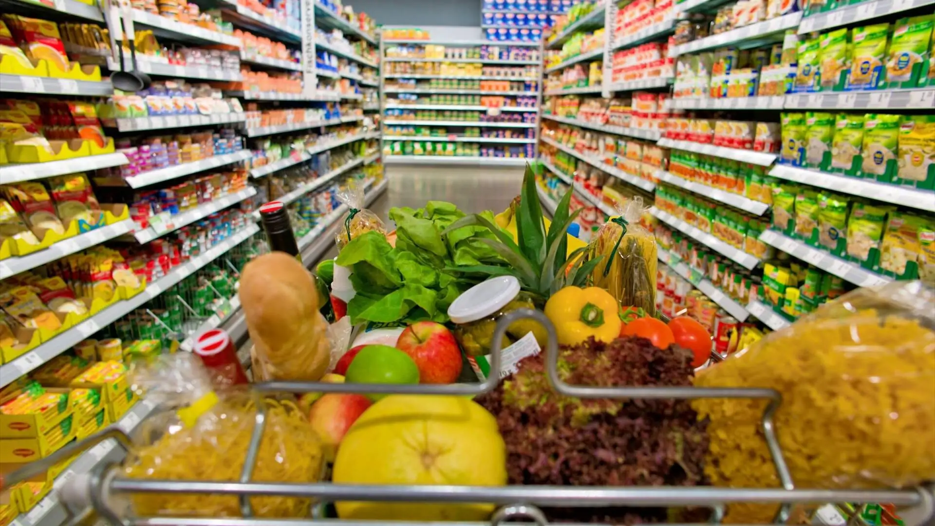 Einkaufswagen im Supermarkt zwischen zwei Regalen symbolisiert die Intralogistik im Lebensmittelhandel