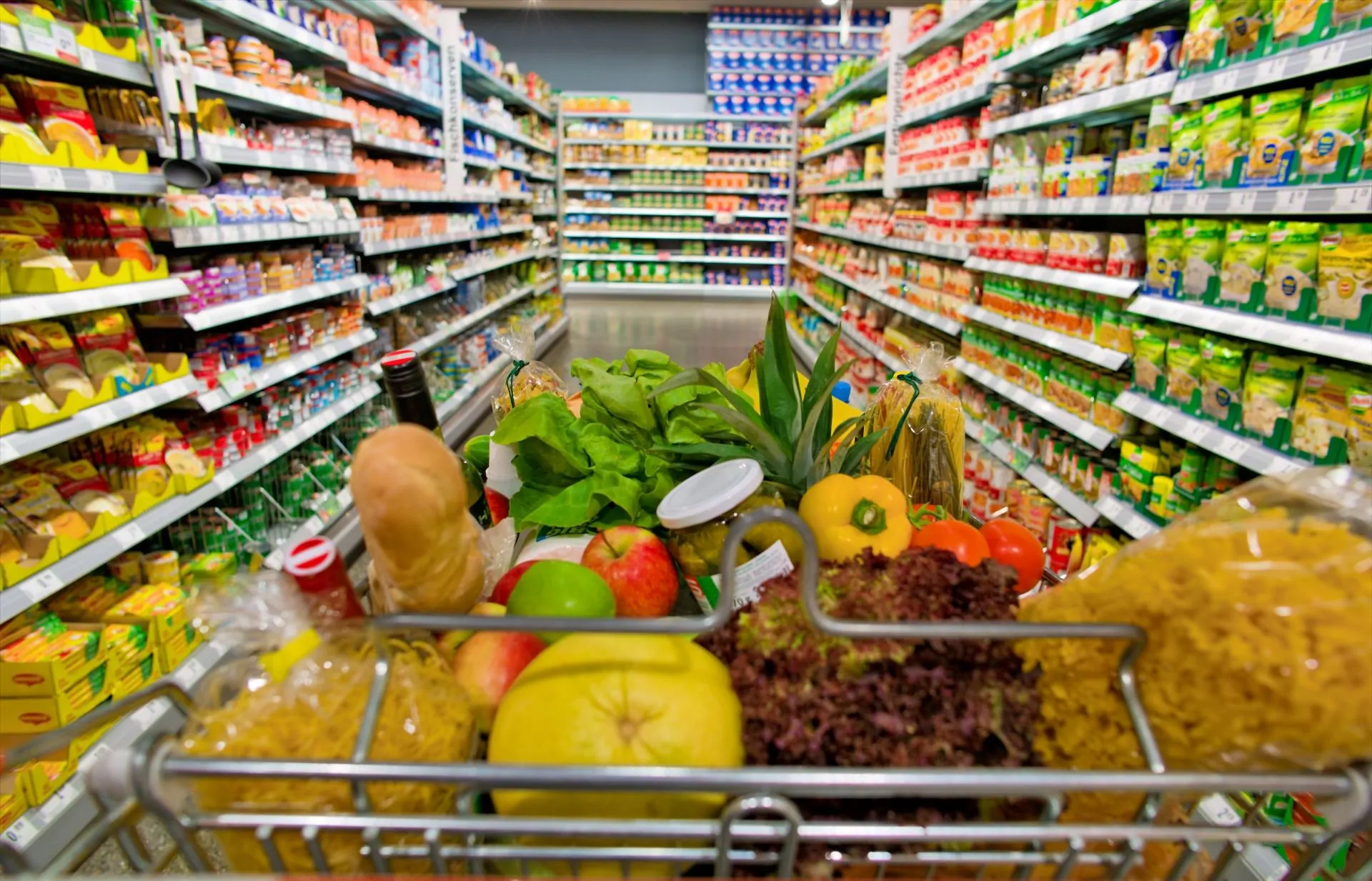 Einkaufswagen im Supermarkt zwischen zwei Regalen symbolisiert die Intralogistik im Lebensmittelhandel